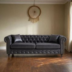 a black leather couch sitting on top of a hard wood floor next to a window