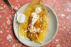 a white plate topped with corn on the cob covered in toppings next to a spoon