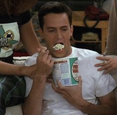 a man sitting on a couch holding a box of cereal with his mouth covered in marshmallows