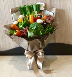 a bouquet of fresh vegetables wrapped in brown paper with a bow on the end, sitting on a tile floor