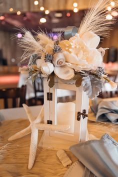 a small white lantern with flowers and feathers on the table at a wedding or reception