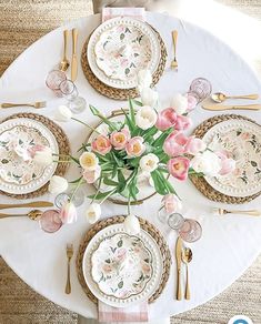 a white table topped with lots of pink and white flowers next to gold place settings