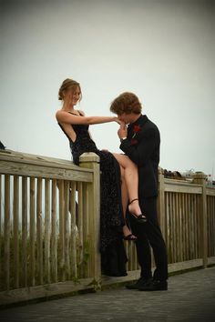 a man in a tuxedo leans over a woman's shoulder on a wooden fence