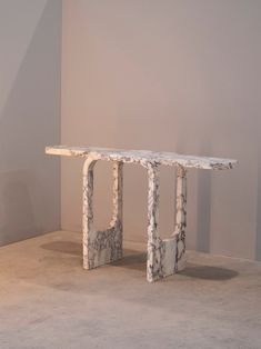 a marble table sitting on top of a floor next to a gray wall and white walls