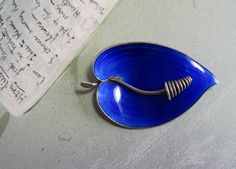 "Here's a pretty sterling and blue enamel brooch made in Norway, and signed with Einar Modahl's mark on the back.  It has a modernist flower (calla lily?) design and measures 2\" across.  It is in excellent condition with no damage'.  Please see the picture with a coin for size comparison, as items may appear larger than they actually are.  This is necessary to provide accurate details.  Thanks for looking.  And thank you for shopping sustainably." Collectible Hallmarked Blue Brooches, Blue Enamel Brooch Gift, Blue Enamel Brooch For Gift, Blue Enamel Brooches For Gift, Collectible Blue Enamel Pin, Blue Enamel Collectible Pin, Lily Design, Leaf Brooch, Enamel Brooch