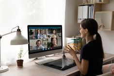 a woman sitting at a desk in front of a computer with people on the screen