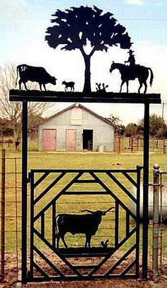 an iron gate with cattle and trees on top in the middle of a grassy field