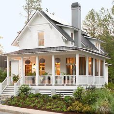 a white house with porches and windows in the front yard, surrounded by greenery