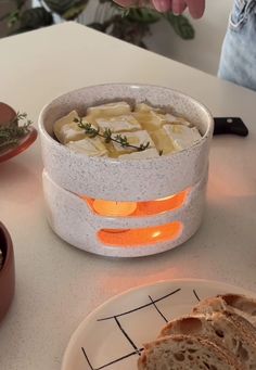 a bowl of food on a table next to a plate with some bread in it