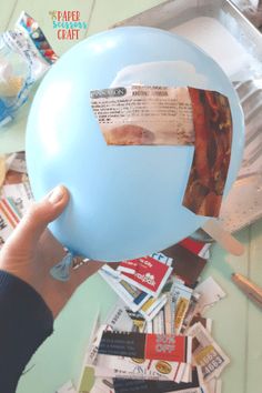 a person holding up a blue balloon with some stickers on it and papers all over the table