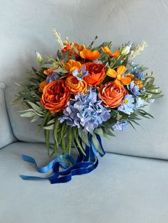 a bouquet of orange and blue flowers on a white couch with a blue ribbon around it