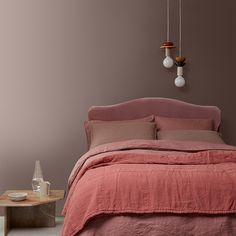 a bed with pink linens and two hanging lights on the wall next to it