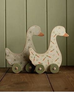 two wooden ducks sitting on top of a wooden table next to each other with wheels