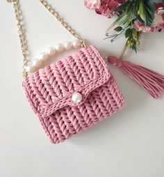 a pink purse with pearls hanging from it's side and a flower in the background