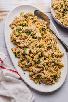 pasta with chicken and parsley on a white plate next to a red striped napkin