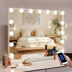 a person holding a cell phone in front of a mirror with light bulbs on it