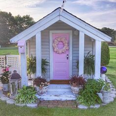 a pink door sits in front of a small house with potted plants and flowers