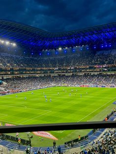 a stadium filled with lots of people watching a soccer game on the field at night