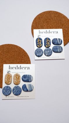 two business cards with blue and gold buttons on them next to a cork board circle