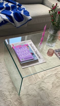 a glass coffee table with magazines and flowers on it