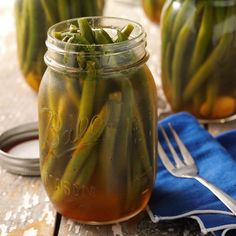 three jars filled with pickles sitting on top of a table next to a fork