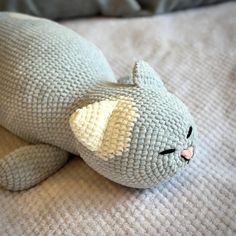 a crocheted gray cat laying on top of a white bed sheet with eyes closed