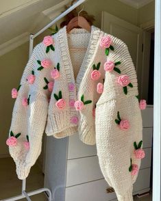 a white sweater with pink roses on it hanging from a clothes rack in a closet