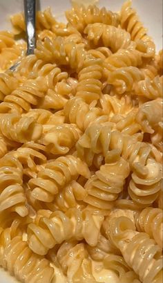 a bowl filled with macaroni and cheese on top of a table next to a fork