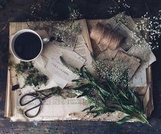 an old book with flowers, scissors and other items on it next to a cup of coffee