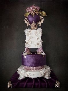 a three tiered cake with purple and white decorations on the top, in front of a black background