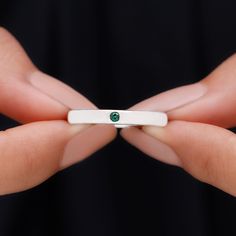 a woman's hands holding a white ring with a green stone