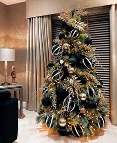 a christmas tree decorated with black and gold ornaments in a living room area next to a window