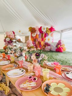 a table set up for a party with pink plates and flowers in vases on it