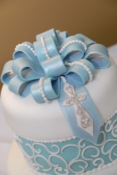 a blue and white cake decorated with pearls, bows and a cross on the top