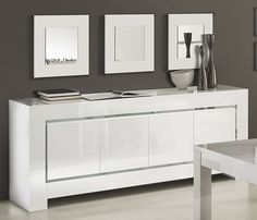 a modern white sideboard with three pictures on the wall and two vases next to it