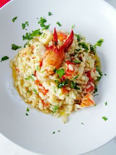 a white plate topped with riso and rice covered in lobsters, garnished with parsley