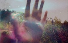 a blurry image of someones hand reaching out to the sky with trees in the background