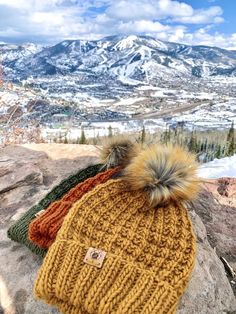 two knitted hats sitting on top of a rocky cliff with mountains in the background