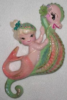 a little mermaid holding a baby doll on top of it's back in the shape of a sea horse