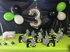 the table is set up with black and white checkered paper, green balloons, and race cars