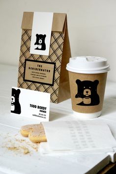 a cup of coffee next to a bag and some cookies on a white tablecloth