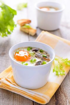 a white bowl filled with soup on top of a wooden table next to a napkin