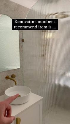 a hand pointing at a white bowl on top of a counter next to a mirror