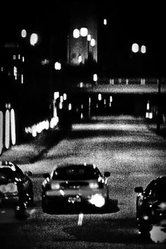 black and white photograph of cars driving down the road at night time with lights on