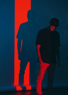 a man standing in front of a red and blue wall with his shadow on it