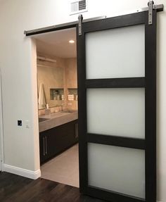 an open sliding door in a kitchen with wood floors and white walls, leading into the bathroom