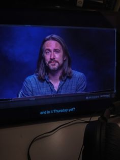 a man with long hair is on a television screen and has headphones around his neck