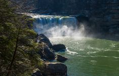 the water is green and blue as it pours into the river from behind some rocks