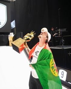 a man holding a trophy in his right hand while wearing a green and gold scarf