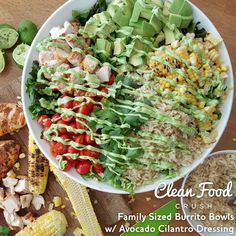 a bowl filled with lots of food on top of a wooden table next to sliced corn